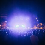 A lively outdoor concert scene at night with colorful lights and a large audience.